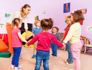 A group of kids hold hands together with their day care teacher.