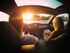 Two people ride in a car together as the sun shines through the front window.