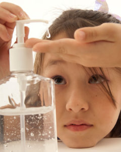 A young girl applies hand sanitizer to her hand.