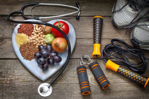 A heart-shaped plate is filled with fruit, nuts and vegetables and is placed next to a jump rope, tennis shoes and a stethoscope.
