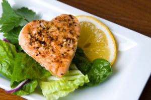 A heart-shaped piece of salmon is shown on a plate with lettuce and lemon.