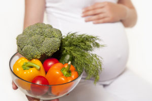 A pregnant woman holds a bowl of vegetables.