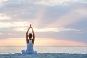 A woman participates in yoga outside near a beach.