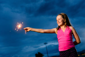 A young girl holds a firecracker and dangles it in the air.
