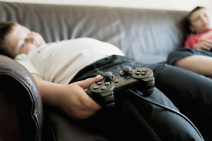 A young boy holds a remote controller and lounges on a couch.