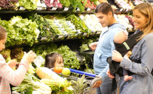 A family grocery shops together and navigates the produce aisle.