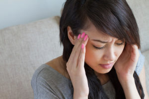 A woman holds her head with her hands and appears to be having a migraine.