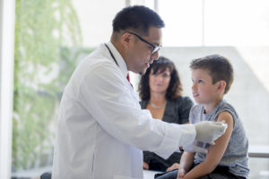 A medical professional rolls up a child's sleeve to give him a vaccine.