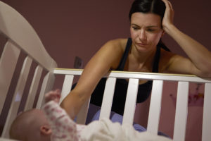 A mother comforts her newborn baby by placing her hand inside a crib.