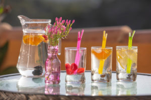 A pitcher of infused water is shown next to three full glasses of infused water. Each glass has a colorful straw.