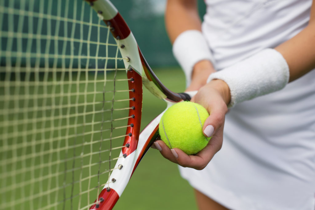 A woman holds a tennis ball and racket.