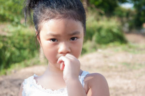 A young girl bites her nails as she stands outside.