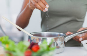A woman sprinkles salt into a pan while she cooks.