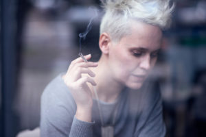 A woman holds a cigarette and appears to be smoking.