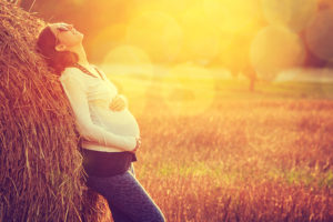 A pregnant woman lies against a bushel of hay.
