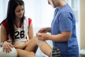 An athletic trainer wraps a volleyball player's knee with compression wrap.