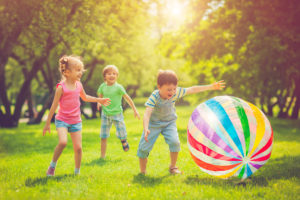 Three kids play together outside with a large ball.