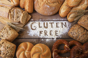 A table is filled with different types of whole grains. A pile of flour is shaped to spell out, "Gluten Free."