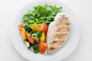 A meal from the DASH diet is shown. A white plate holds a chicken breast and grilled vegetables.