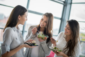 Three women eat a salad together during their lunch break.