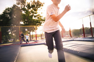Young kids jump on a trampoline at a park.