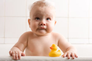 A baby sits in a bath tub with a rubber duck.