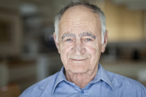 An elderly man poses for a photo and smiles.