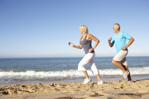 Two adults jog along the beach together.