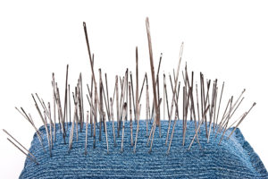 Pins and needles are attached to a blue pillow.