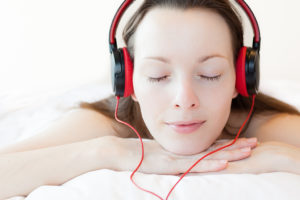 A woman lies on a bed and listens to music through headphones.