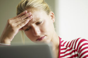 A woman rests her head against her hand as she stares into a laptop. She appears stressed.