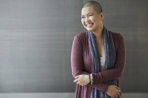 A woman with no hair smiles as she crosses her arms.