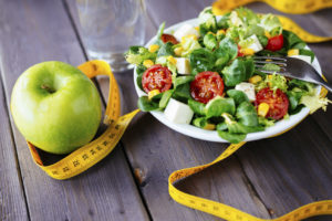 A salad and a green apple is shown next to measuring tape.