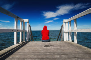 A woman sits on a pier and looks out at the ocean.