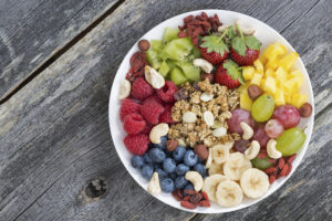 A plate contains blueberries, bananas, pineapple, strawberries, raspberries, kiwi, grapes, granola and nuts.