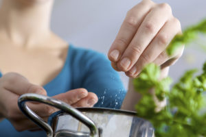 A woman adds a pinch of salt into a pot while she cooks.