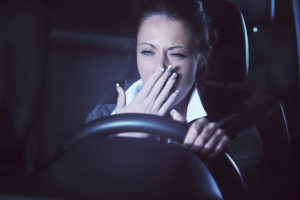 A woman yawns into her hand as she drives a car.