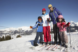 Two adults and two kids pose for a photo outside in the snow. They all appear to be skiing.