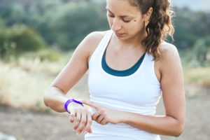A woman athlete looks at her purple wristband for fitness data.