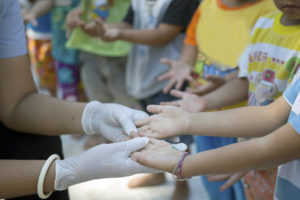 A person wearing gloves looks at children's hands.