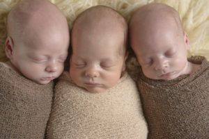 Three babies lie next to each other and are asleep.