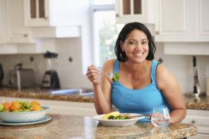 A woman eats a salad in her kitchen and smiles.