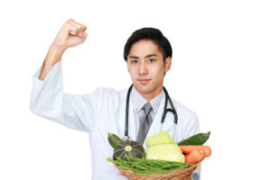 A registered dietitian is shown holding a basket of vegetables and flexing his right arm.