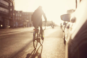 A person rides a bike through a city next to cars.