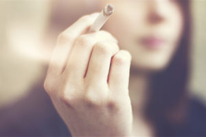 A woman holds a cigarette between her fingers.