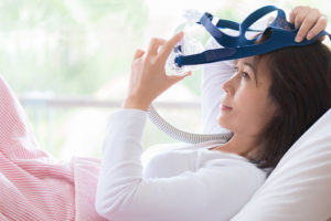 A woman puts on a CPAP machine as she lies in bed.