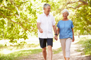 An elderly couple holds hands and walks outside.