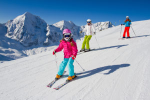 Three kids ski down a snowy slope.