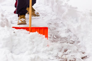 A person shovels snow off of the sidewalk.