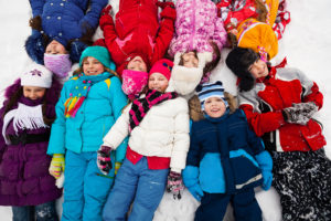 A group of kids lie in the snow together wearing their winter clothes.